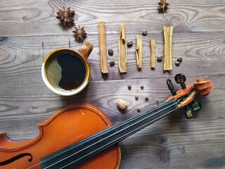 Musical note chord of cinnamon, coffee beans, star anise, with cup of coffe and violin on brown wooden background, top view