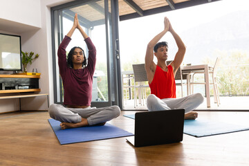 Happy biracial lgbt male couple doing yoga in living room, meditating