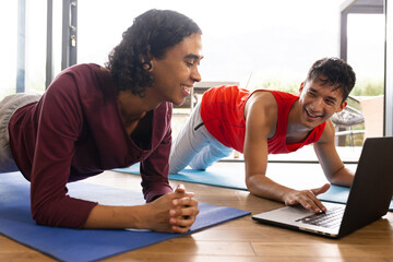 Happy biracial lgbt male couple doing yoga in living room, stretching