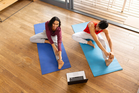 Happy biracial lgbt male couple doing yoga in living room, stretching