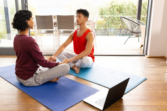 Happy biracial lgbt male couple doing yoga in living room, meditating