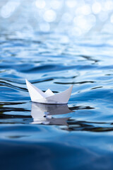 white paper ship on blue water, vertical frame, origami boat floats on the waves, concept of...