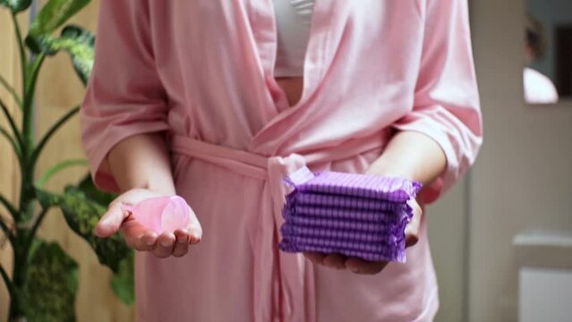Woman in compares menstrual cup, pads. Different types of feminine menstrual hygiene products such as panty liners, cups. On hands, stack of pads, silicone menstrual cup compared. Zero waste concept