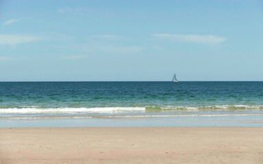 Fototapeta na wymiar Breezy ocean view with clean sandy coastline and a boat on the horizon 