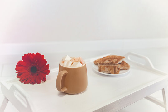 light photo with breakfast, coffee with marshmallows, green apple, red flower and pancakes on a white tray, blurred background, selective focus, close-up, warm tinting