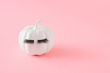 White Halloween pumpkin with eyelashes on pink pastel background. Minimal Holiday season concept.
