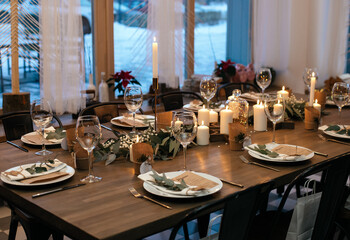 Christmas evening. Stylish table design. Serving with candles, eucalyptus, garlands and white plates