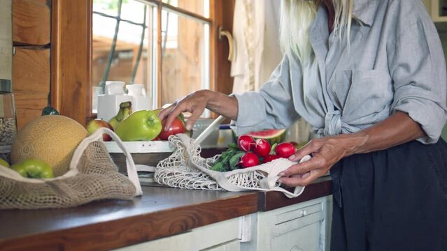 Senior woman unpacking local food in zero waste packaging from bag in kitchen at home.