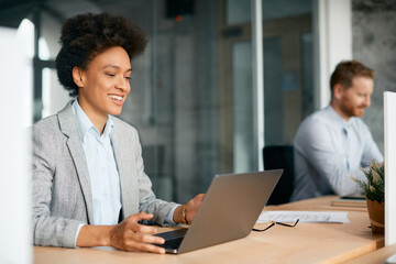 Fototapeta premium Happy black businesswoman works on laptop in office.