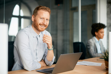 Obraz premium Happy businessman working on laptop and looking at camera.