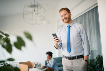 Happy entrepreneur using mobile phone in office and looking at camera.