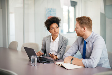 Black female CEO using laptop while talking to colleague in office.