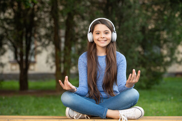 Meditating while listening to music. Happy teenage girl meditating on bench outdoors, meditating.