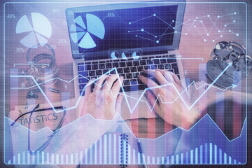 Double exposure of man's hands typing over laptop keyboard and forex chart hologram drawing. Top view. Financial markets concept.