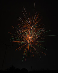 Several bursts of fireworks with rays of orange and green light from the center and many sparks on a black background