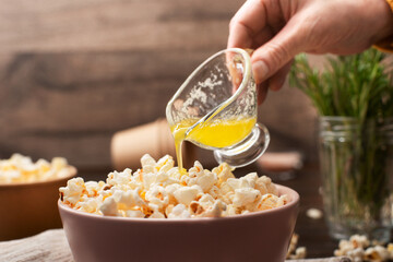 Melted butter being poured on popcorn in clay bowl on kitchen table