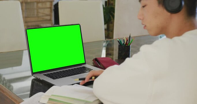 Video of asian boy with headphones having online lessons on laptop with copy space