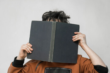 little boy hides his face behind a book