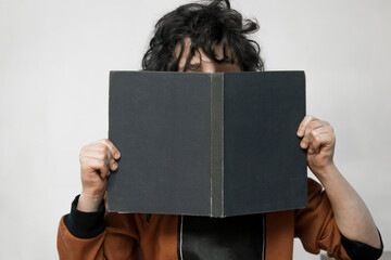 little boy hides his face behind a book