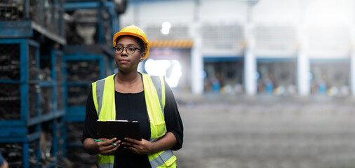 Plus size black female worker wearing safety hard hat helmet inspecting old car parts stock while working in automobile large warehouse - Powered by Adobe