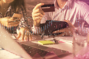 Double exposure of man and woman on-line shopping holding a credit card and forex graph hologram drawing. Stock market E-commerce pay on-line concept.