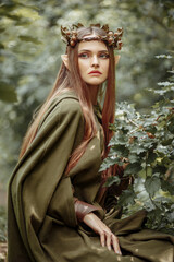 Elf girl in the forest with a green cape and a wreath on her head. Fantasy elf from the forest....
