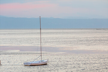 Barca a vela ormeggiata nella laguna del mare adriatico, isola della citt&agrave; di Grado. Paesaggio marino all'alba con visibili le montagne alle prime luci del sole.
