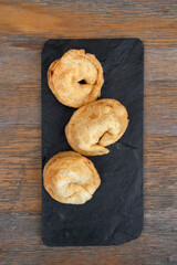 Traditional cheese and ham fried empanadas. Top view of three stuffed pies in a black dish on the wooden table.