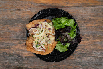 Top view of a milanesa, breaded beef with crumbs, and a fresh salad in a black dish on the...