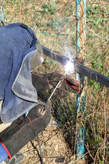 Worker welds metal pipes with electrode welding outdoors