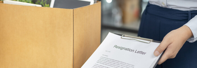 Fototapeta premium Female employee submits her resignation letter and packs her work equipment in a box to prepare to move to work, Can't bear the burden or pressure, Employment contract is expired.