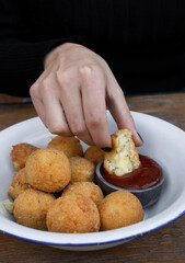 Eating cheese balls at the restaurant. Closeup view of a caucasian woman's hand, dipping a potato and mozzarella croquette in sweet chili dipping sauce.