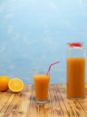 Glass of orange juice, jug and ripe oranges on wooden table