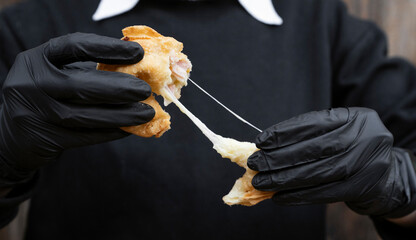 Finger food. Closeup view of a female chef wearing gloves, stretching a traditional cheese and ham...