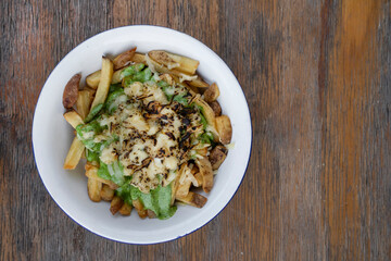 French fries. Top view of a bowl with fried potatoes with spinach cream, mozzarella, cheddar, danvo and blue cheese, in a white bowl on the wooden table.