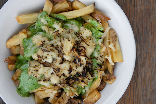 French fries. Top view of a bowl with fried potatoes with spinach cream, mozzarella, cheddar, danvo and blue cheese, in a white bowl on the wooden table.