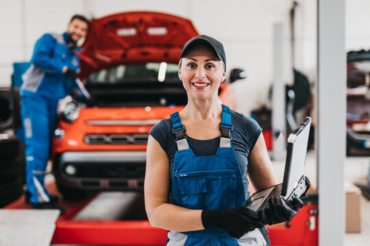 Female and male mechanics working together in large modern car repair service.