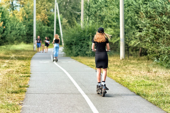 A young woman is riding on the electric scooter in a summer park.