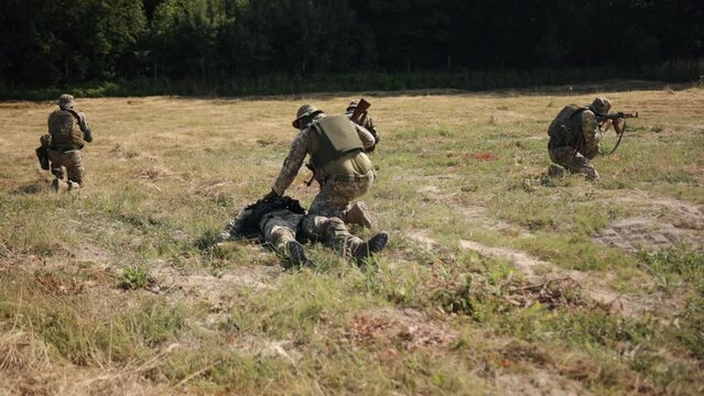 A rescue soldier approaches a wounded warrior and checks for signs of life, while a special unit protects his weapon