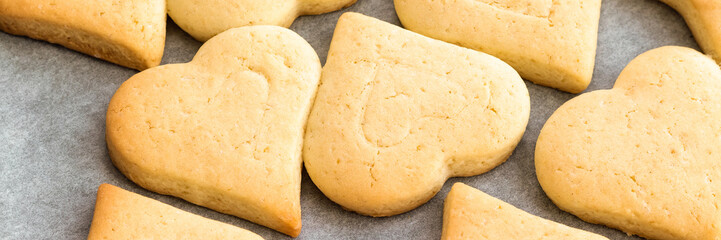 Baked shortbread heart cookies on parchment paper banner. Wide panoramic header. Selective focus