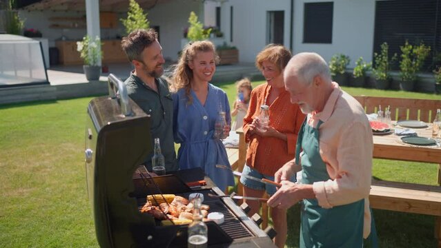 Multi generation family grilling outside on backyard in summer during garden party