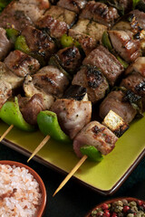 Macro close up of baked meat skewers on a green dish with sage leaves, salt and mixed pepper.