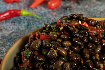 Macro close up of black beans with dried tomatoes and red Cayenne chili peppers in a brown dish.