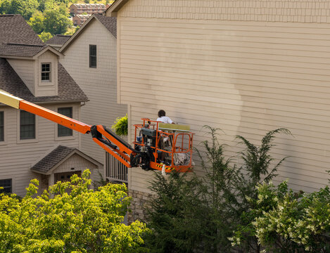 Workman painting the side of a townhouse while standing in an articulating boom lift