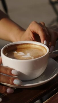 A close up of a hands holding a white cup of coffee