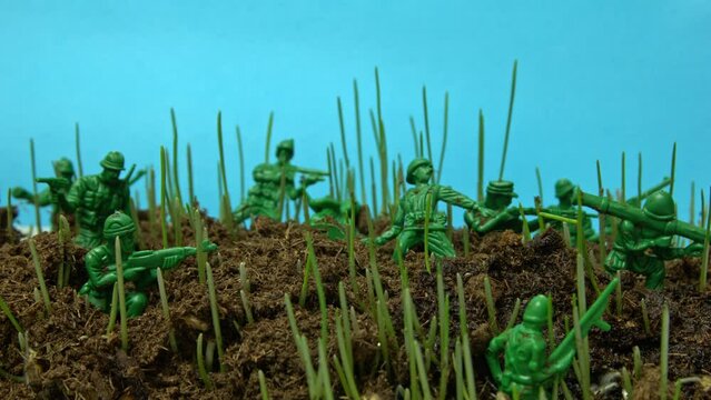 War installation with toy soldiers standing on the ground and grass growing through them in timelapse. Closeup of artificial military holding gun and ready to attack but sprouting plant overthrow them