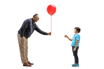 Full length profile shot of a mature man giving a red balloon to a boy