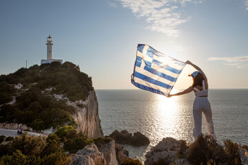 woman with greece flag looking at sunset above the sea
