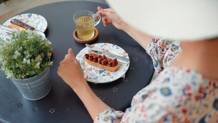 Rear view of young woman in hat drinking a tea with dessert