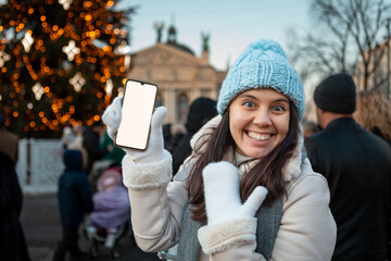 smiling happy woman at christmas city fair holding phone with white screen